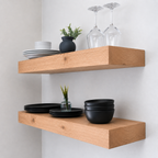 Wooden floating shelves with black dishes and glasses on a white wall