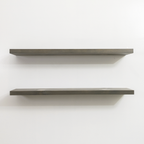 Two gray wooden floating shelves on a white wall