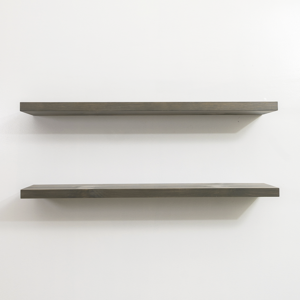 Two gray wooden floating shelves on a white wall