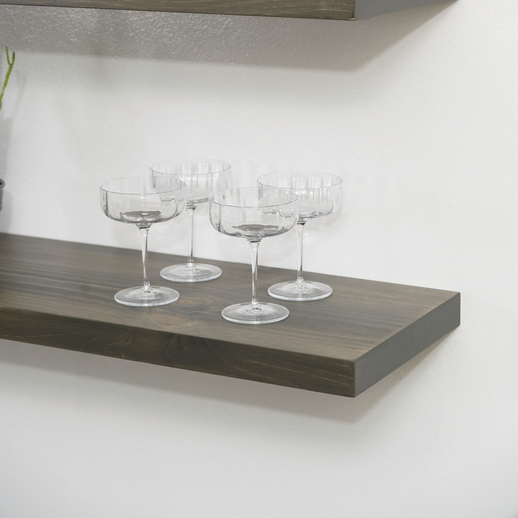 Set of clear glass goblets on a wooden floating shelf against a white wall.