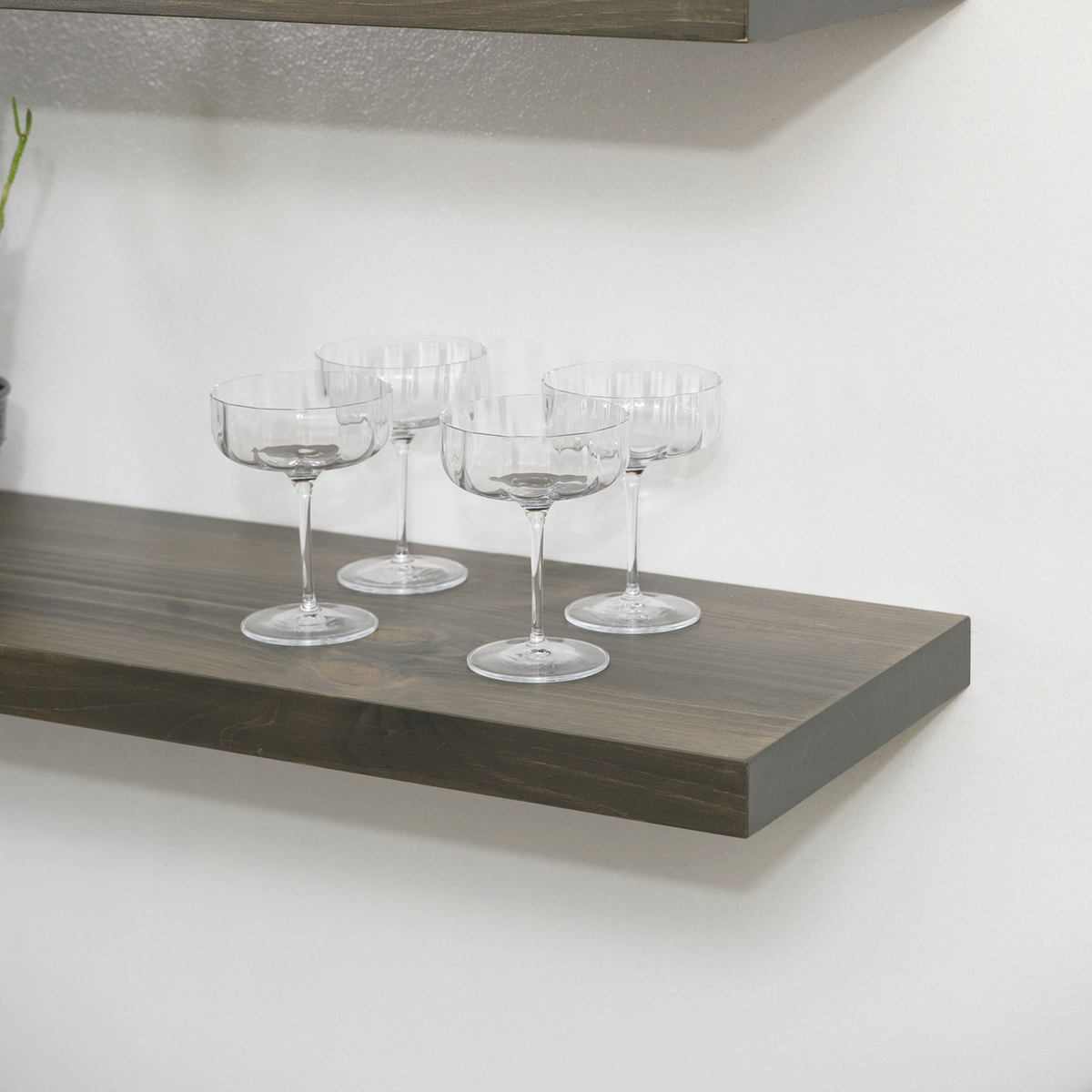 Set of clear glass goblets on a wooden floating shelf against a white wall.