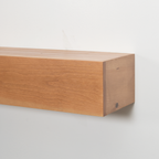 A close-up of a light brown wooden floating fireplace mantel mounted on a plain white wall, showing the wood grain and end grain detail.