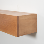 Close-up of a light natural wood floating fireplace mantel mounted against a plain white wall, showing the wood grain and corner construction.