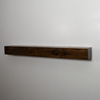 A long, rectangular floating fireplace mantel made of dark brown wood with visible grain, mounted against a plain light gray wall.