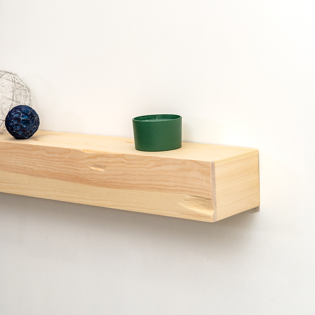 A light natural wood floating fireplace mantel mounted on a white wall, styled with a small dark green cup and a textured blue decorative sphere.