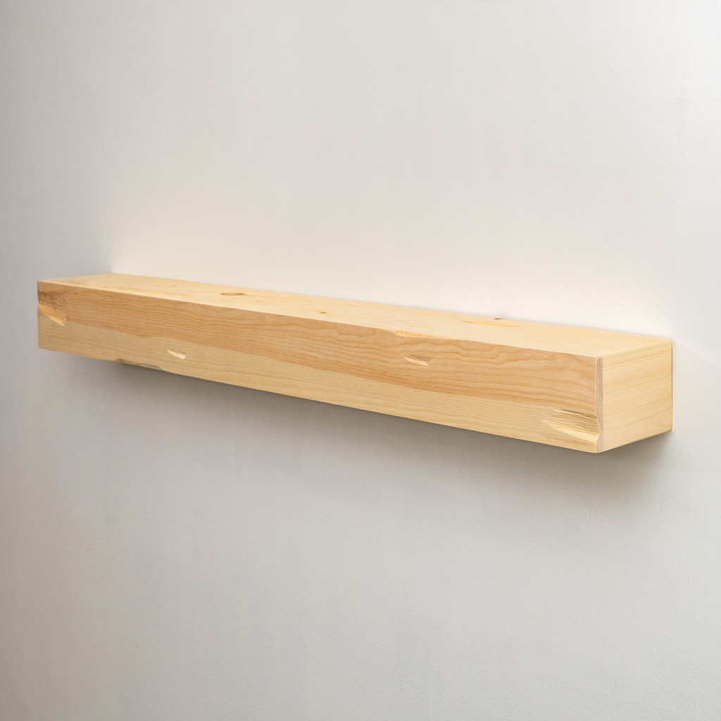A minimalist, long rectangular wooden floating fireplace mantel in a light natural pine finish, mounted on a plain light gray wall.
