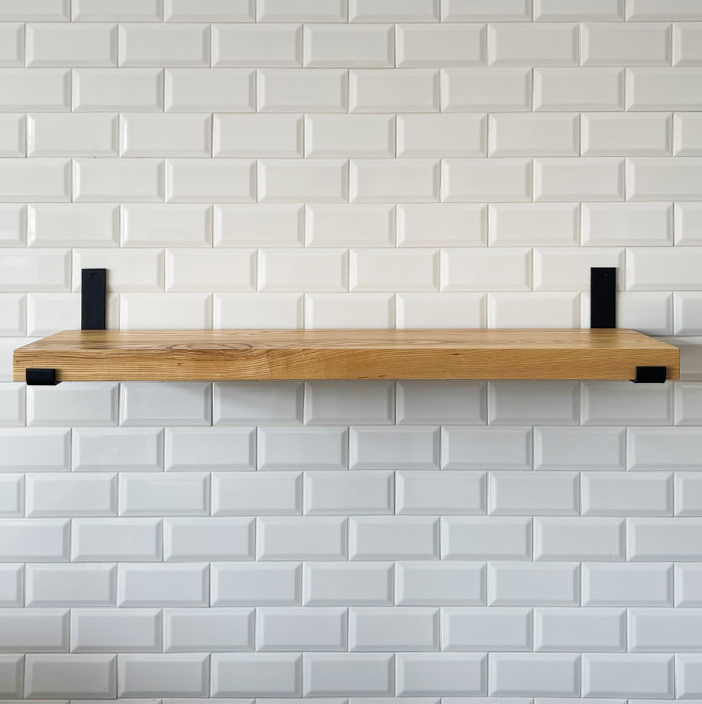 Wooden shelf with black brackets against a white tiled wall