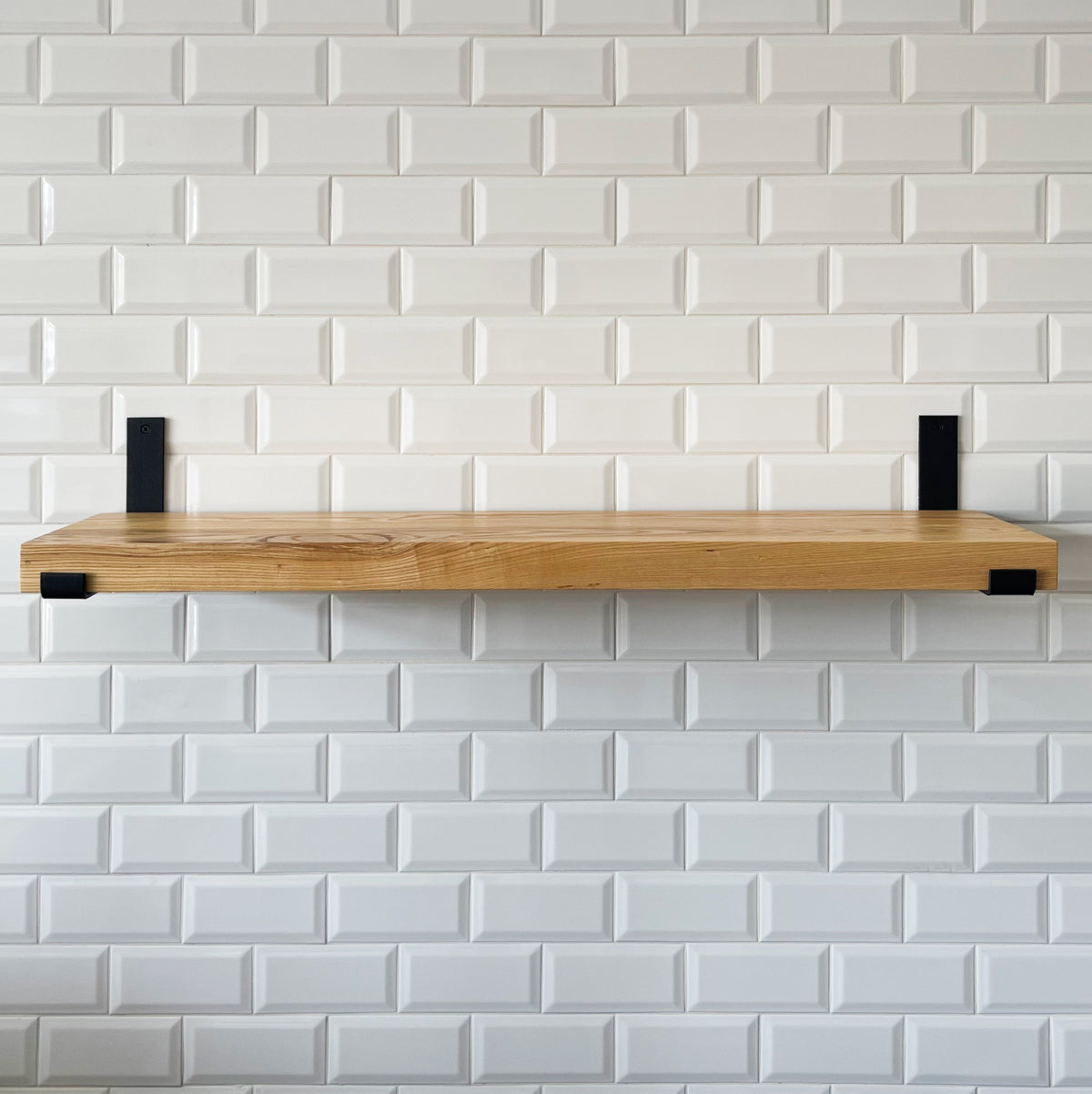 Wooden shelf with black brackets against a white tiled wall
