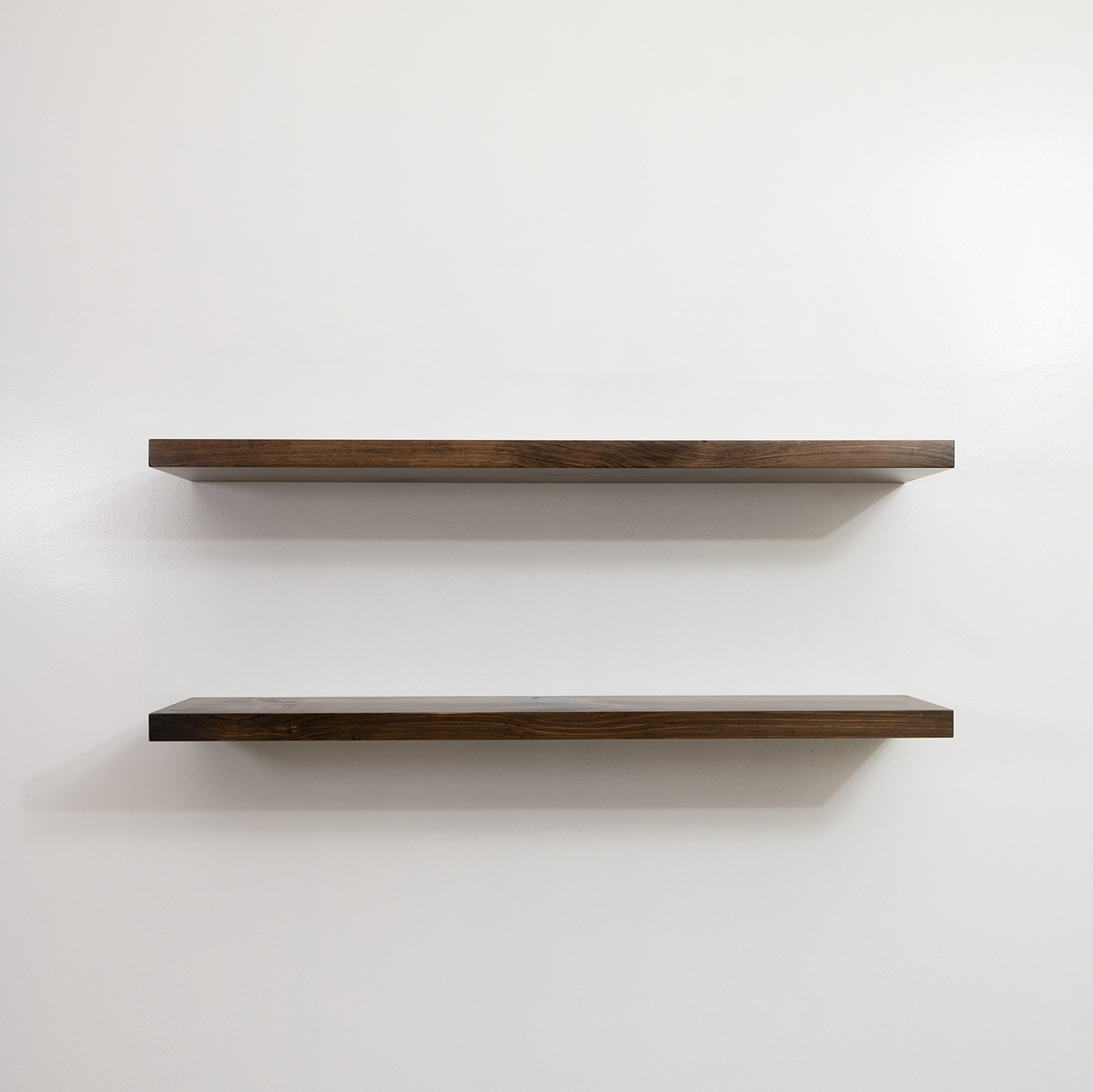 Two wooden floating shelves on a white wall