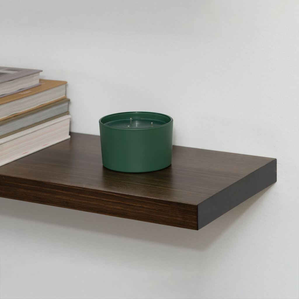 Green pot on a wooden floating shelf with books stacked beside it against a white wall.