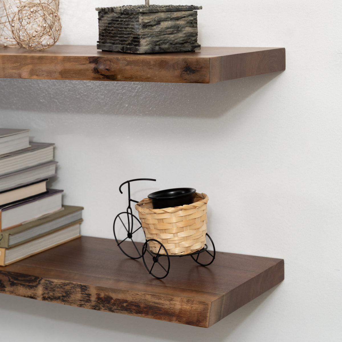 Wooden floating shelves with books, a decorative basket, and a small black bike on a white wall background.