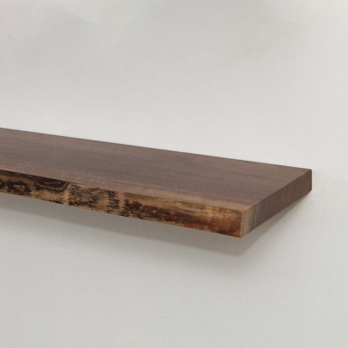 Wooden live edge walnut floating shelf against a white wall