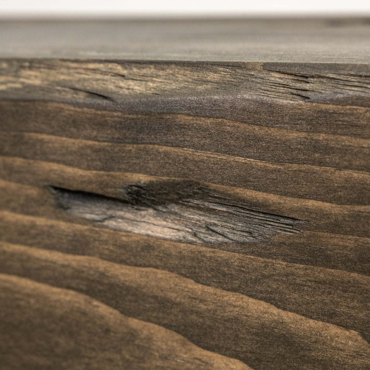 Close-up of a dark brown wood surface with prominent grain, wavy texture lines, and a small knot, photographed in macro detail.