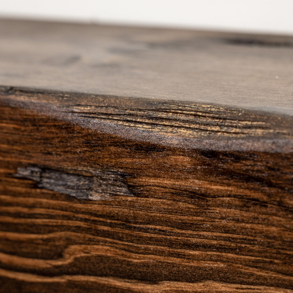 Close-up of a dark brown wood surface with visible grain, knots, and a lighter, smoother wood section above it.