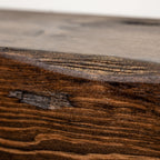 Close-up of a dark brown wood surface with visible grain, knots, and a lighter, smoother wood section above it.