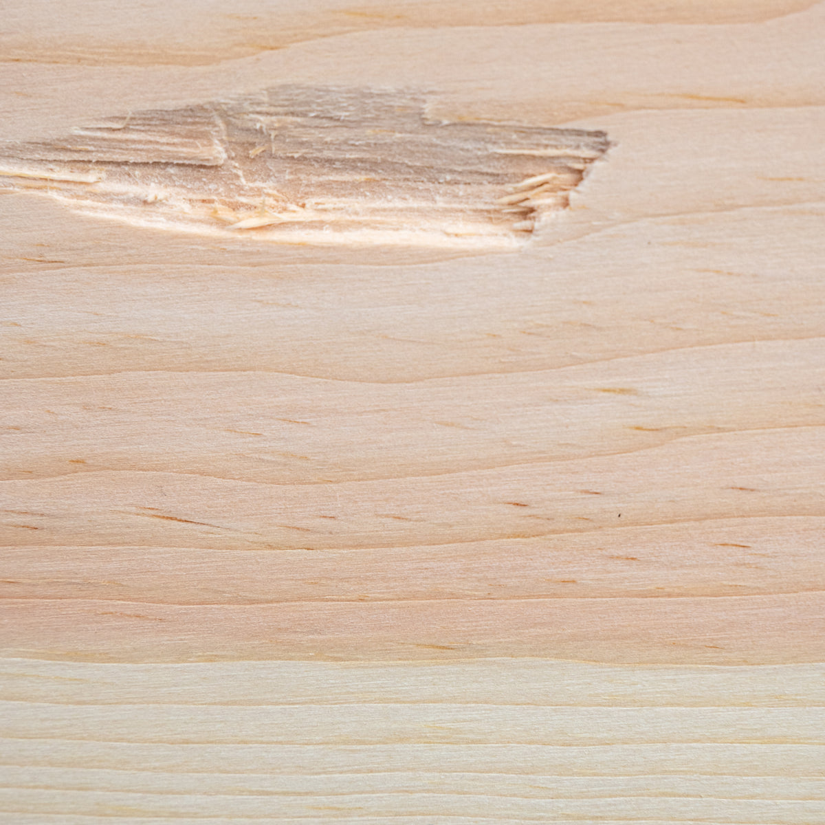A close-up of a light natural wood surface with visible grain, knots, and a slightly rougher patch near the top left.