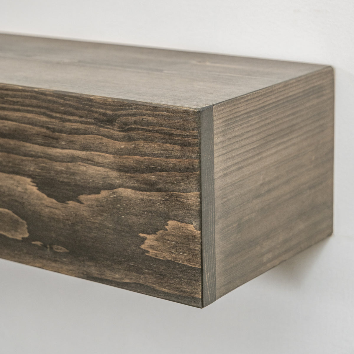 A close-up of a floating wooden fireplace mantel with a dark brown wood grain finish, mounted against a plain white wall.