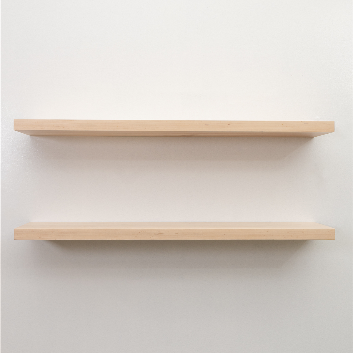 Two maple unfinished wooden floating shelves on a white wall