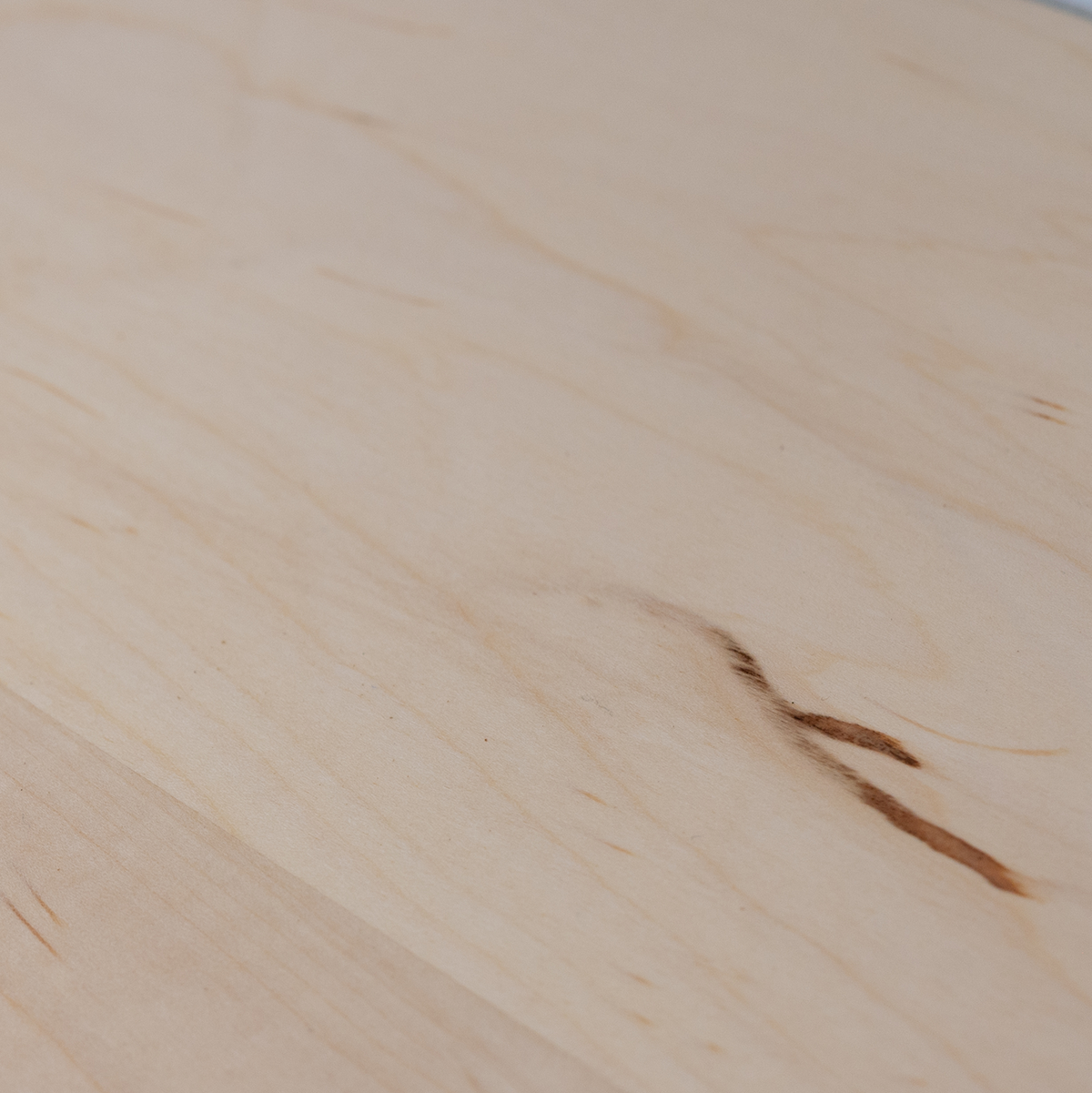 Close-up of a wooden unfinished maple surface with visible grain and a dark knot.