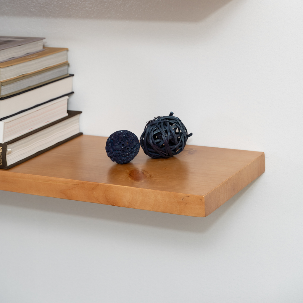 Wooden aged oak floating shelf with books and decorative balls against a white wall