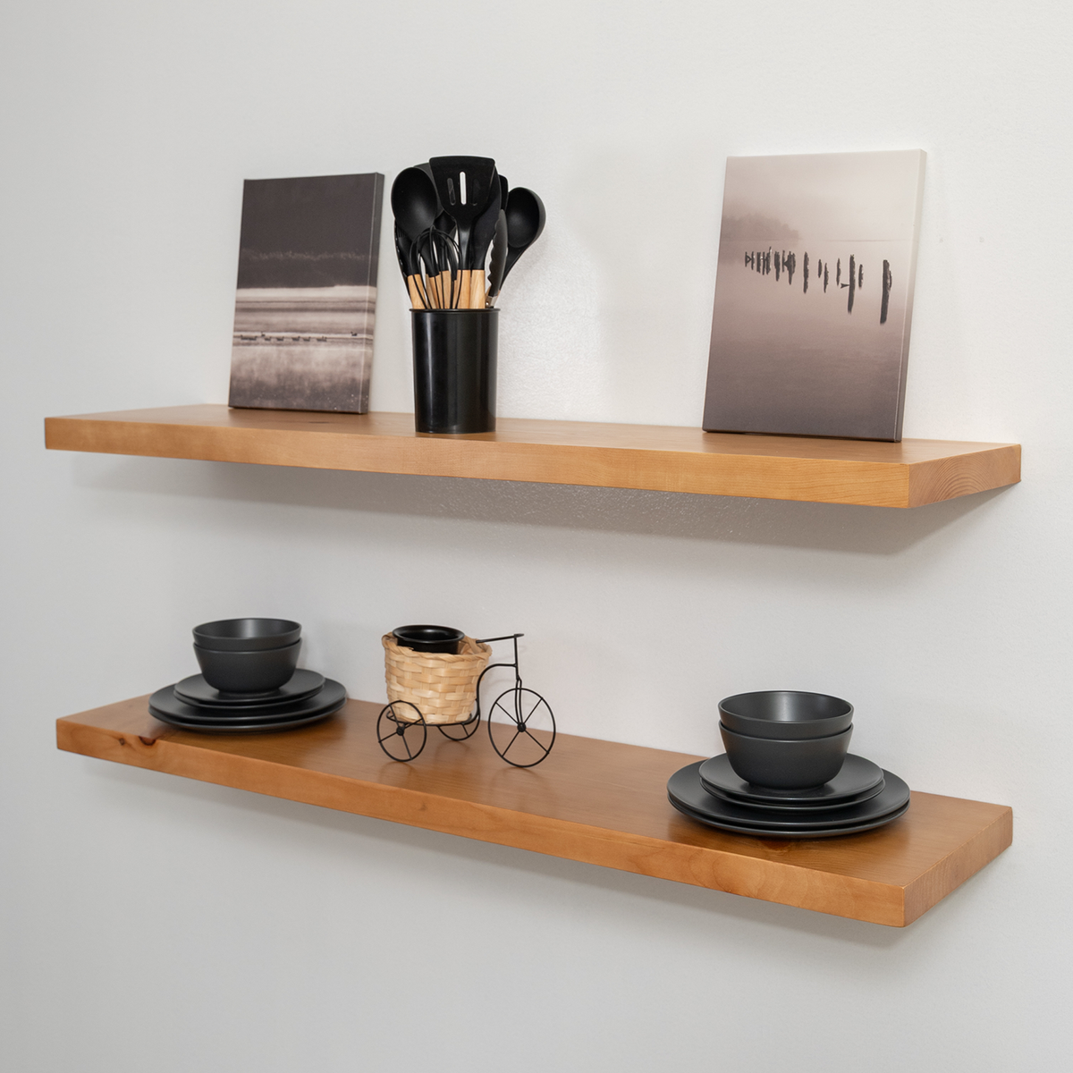 Rustic wooden floating shelves with black bowls, plates, and decorative items against a white wall.