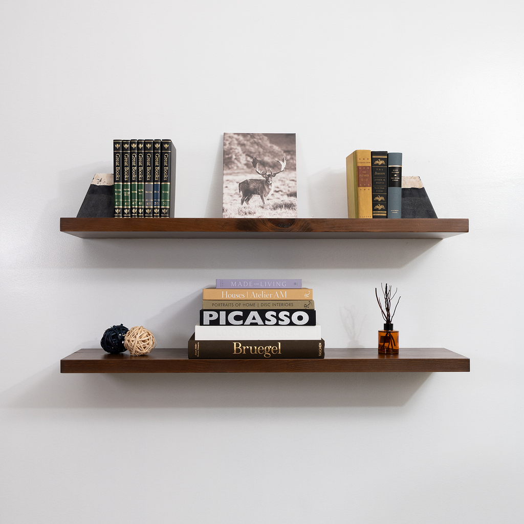 Two wooden floating shelves with books and decorative items against a white wall