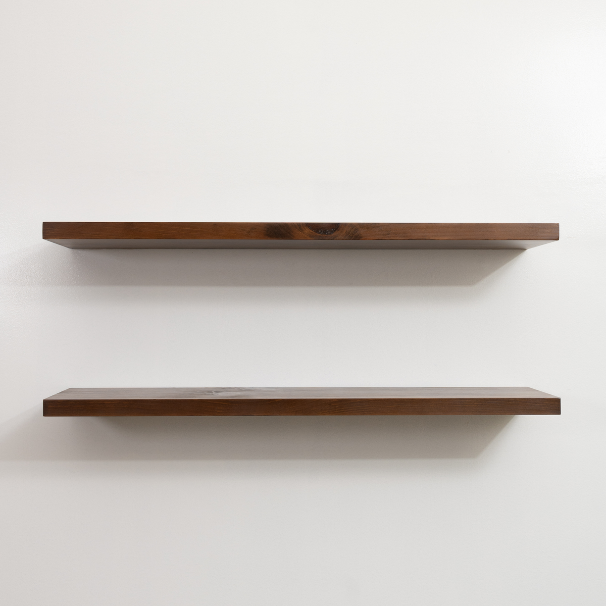 Two wooden floating shelves on a white wall