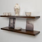 Wooden floating shelf with decorative items including a vase, cups, and a photo frame against a white wall.
