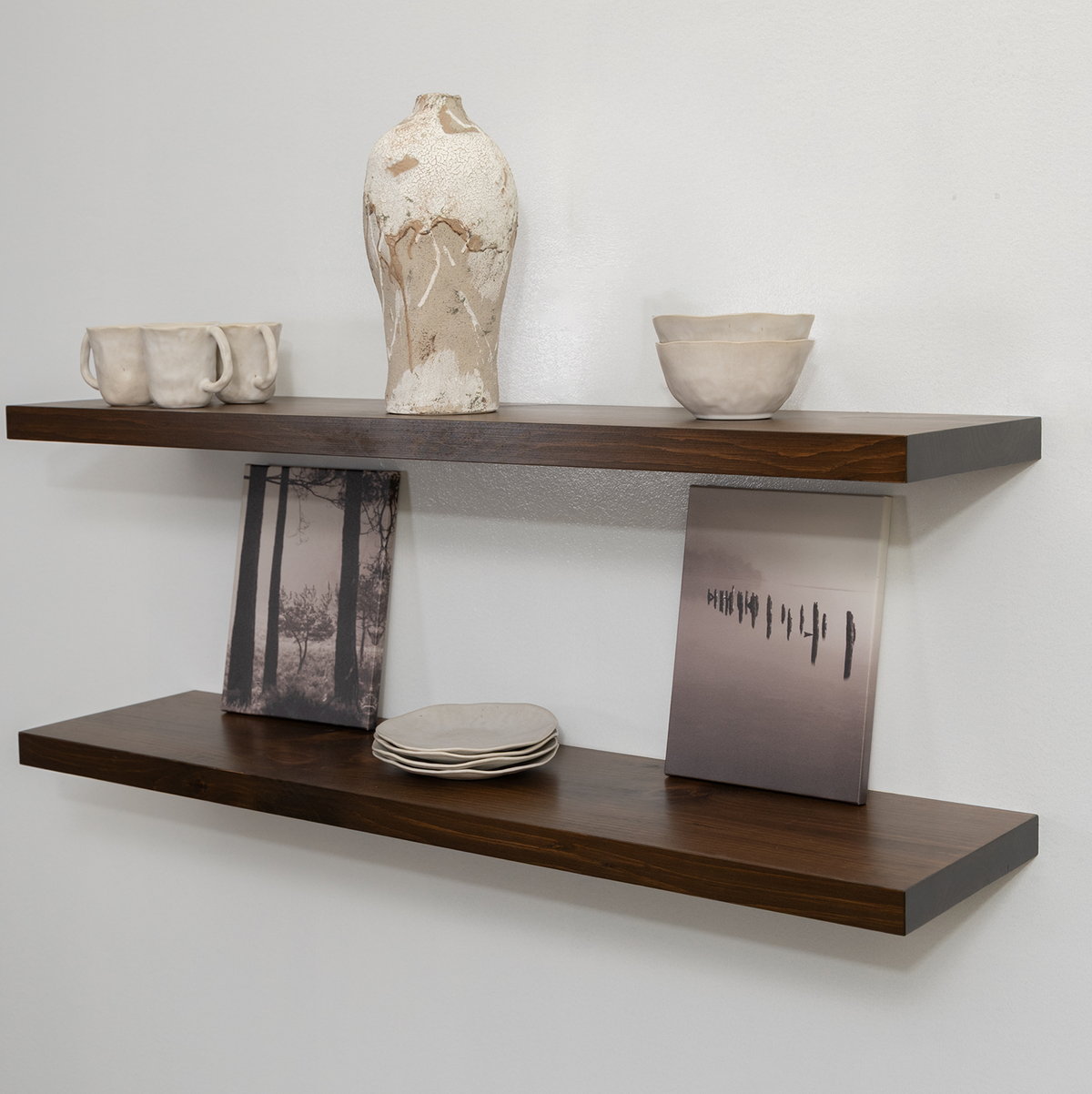 Wooden floating shelf with decorative items including a vase, cups, and a photo frame against a white wall.