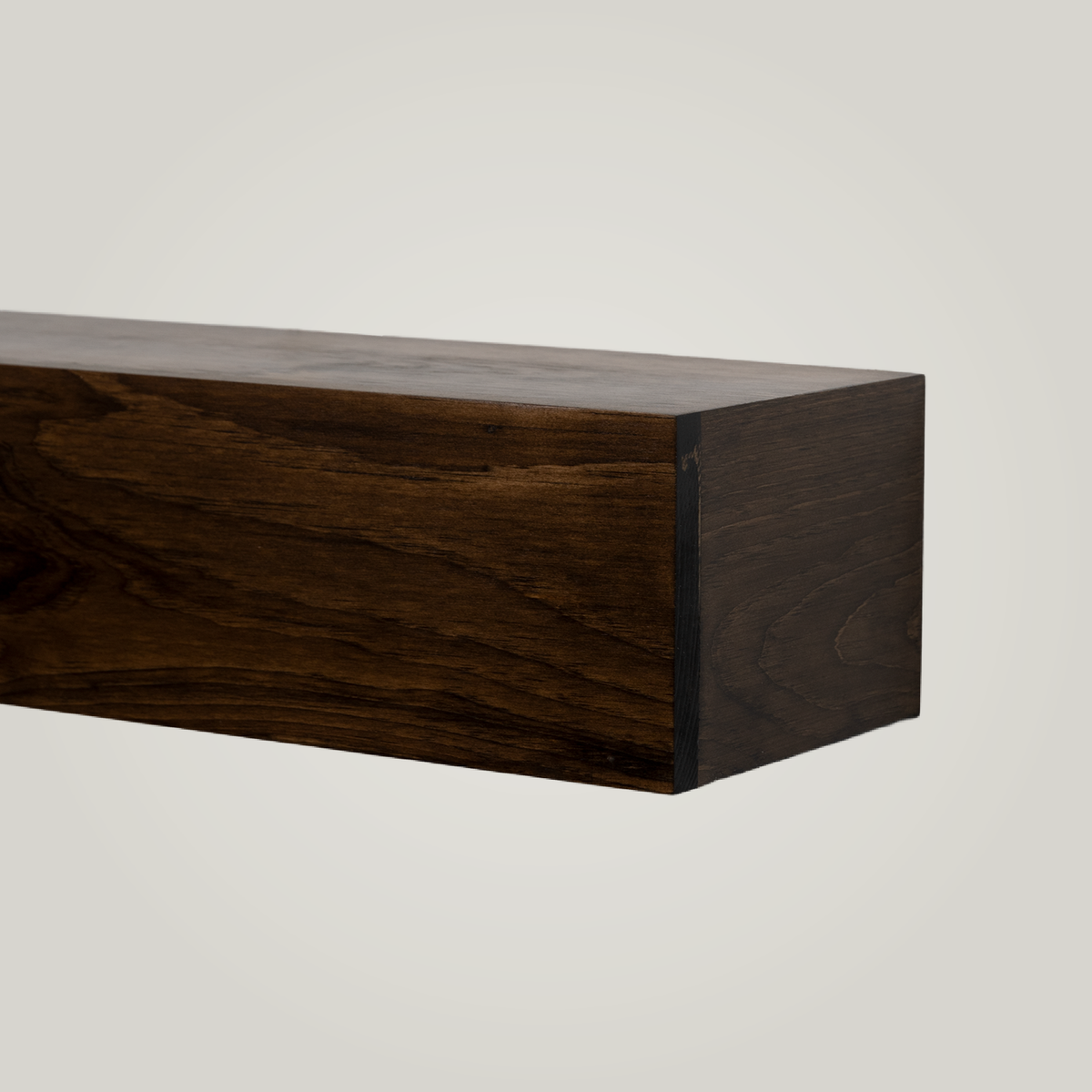 A close-up of a dark brown wooden floating fireplace mantel mounted on a plain white wall, showing the wood grain and end grain detail.