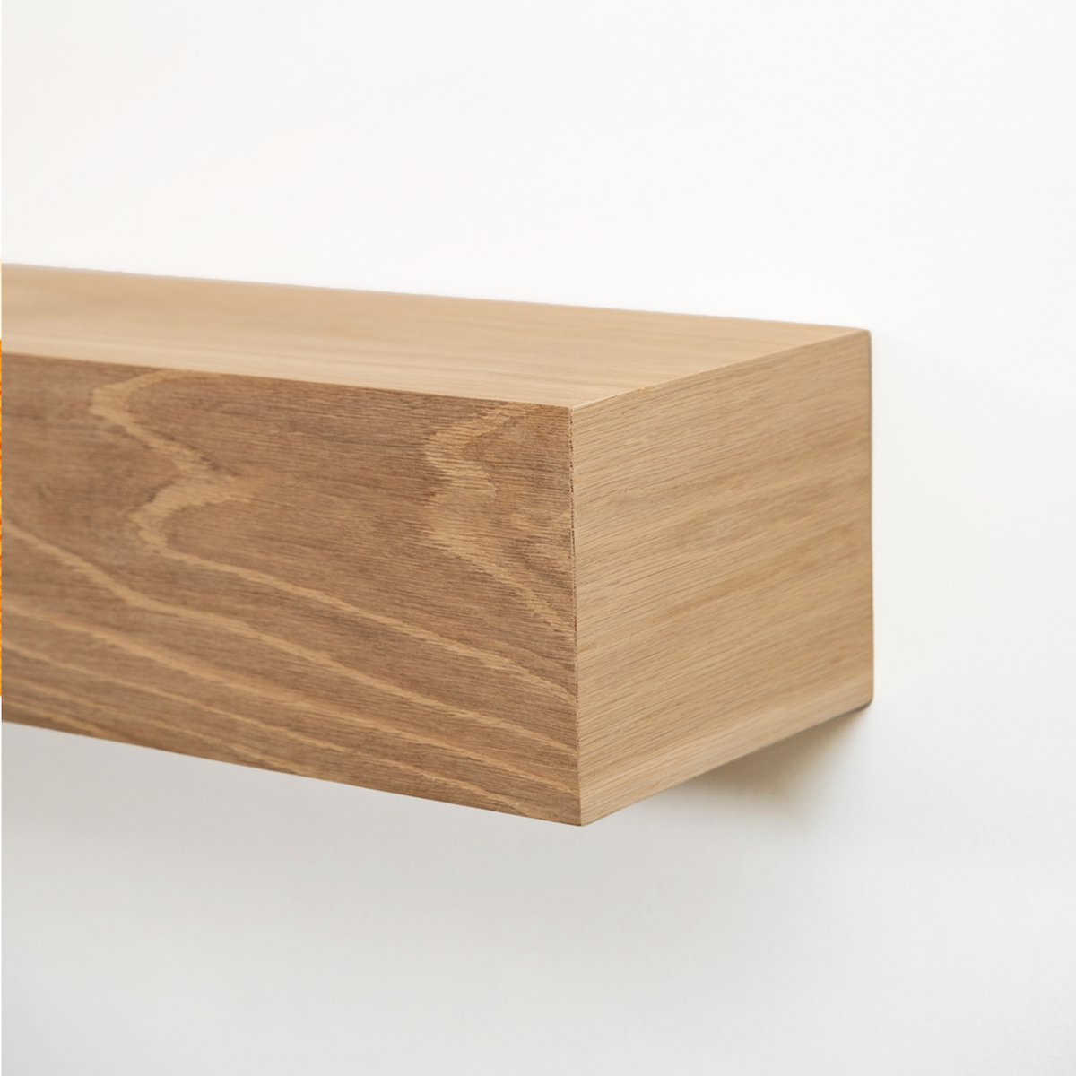 Close-up of a light oak wood floating fireplace mantel mounted on a plain white wall, showing the wood grain and corner detail.