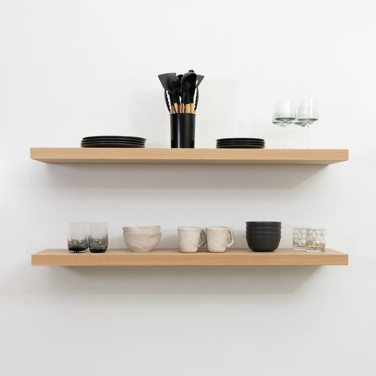 Wooden white oak floating shelves with kitchenware on a white wall