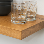Two clear glasses with gold geometric patterns on a white oak wooden floating shelf.