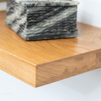 Close-up of a wooden floating shelf end surface with a marble-patterned box in the background