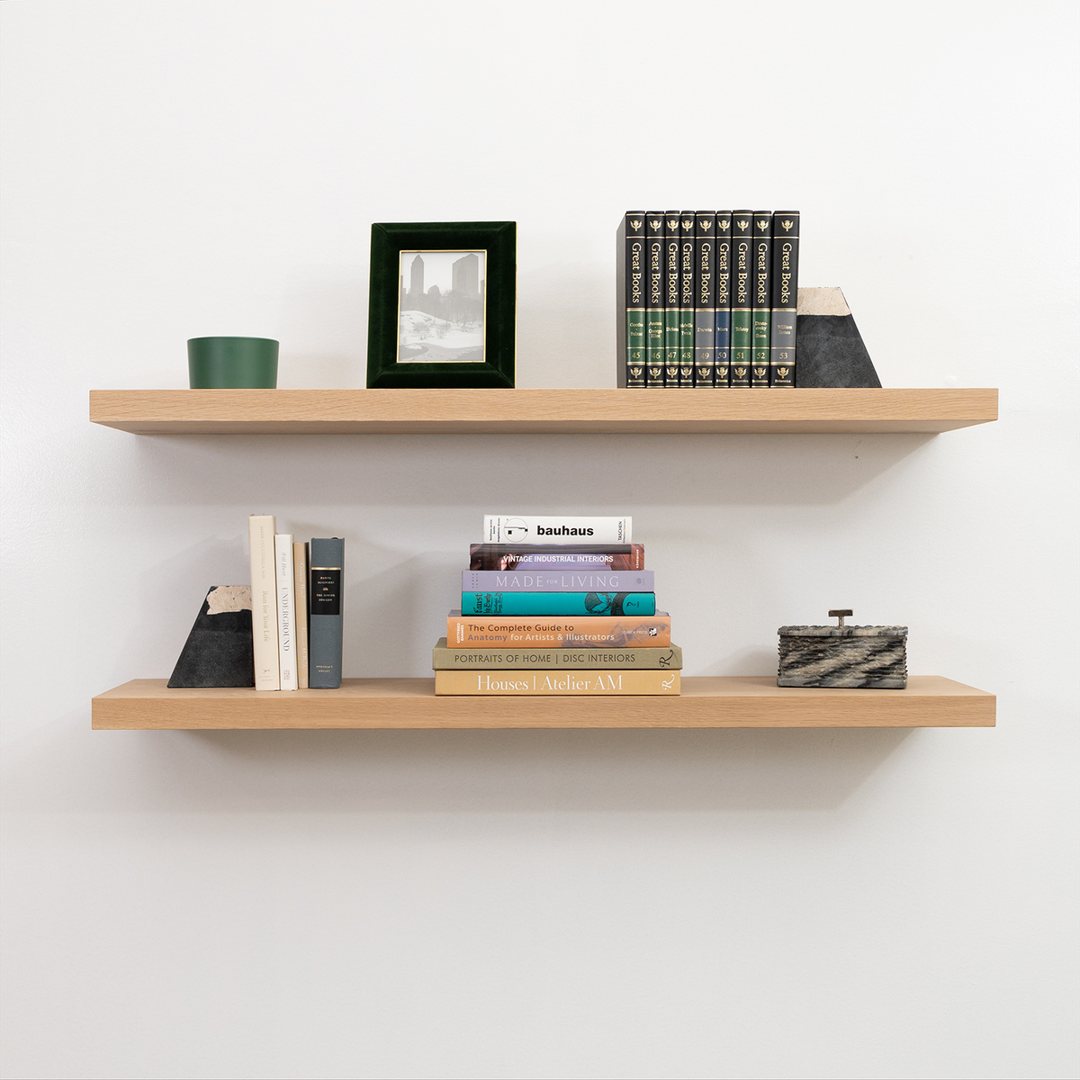 Wooden white oak unfinished floating shelves with books and decorative items against a white wall
