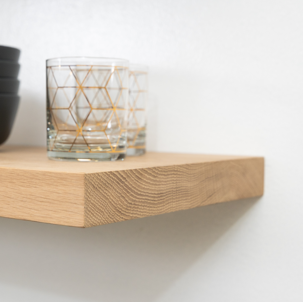 Glass with geometric design on a wooden white oak floating shelf against a white wall