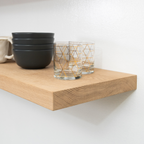 Wooden white oak floating shelf with black bowls and clear glasses with gold geometric patterns on a white background