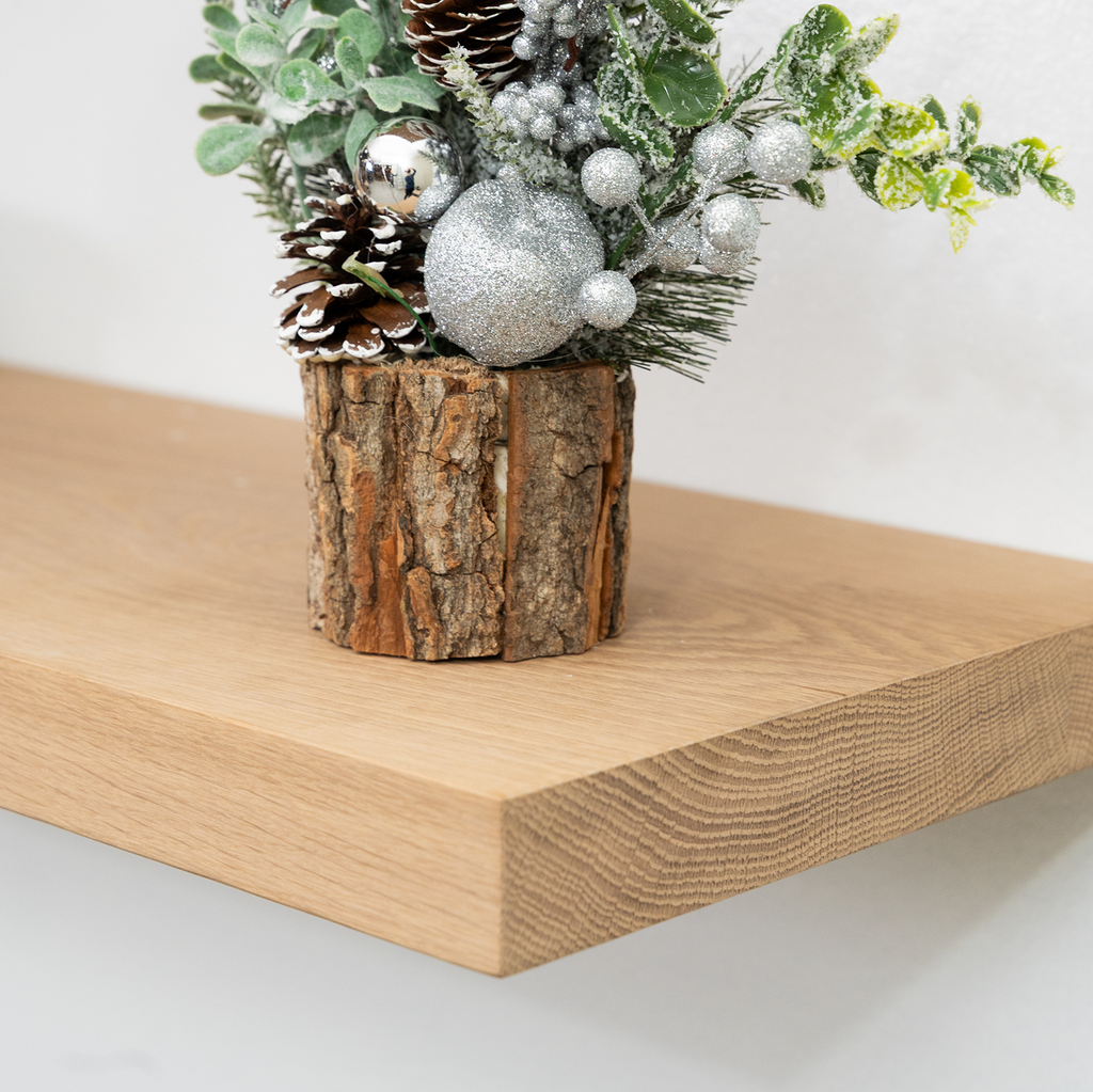 Decorative arrangement with pinecones, silver ornaments, and greenery on a wooden log stand on a wooden floating shelf.