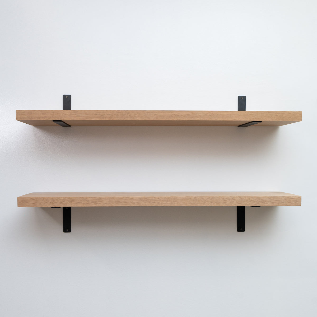 Two wooden shelves with black brackets on a white wall