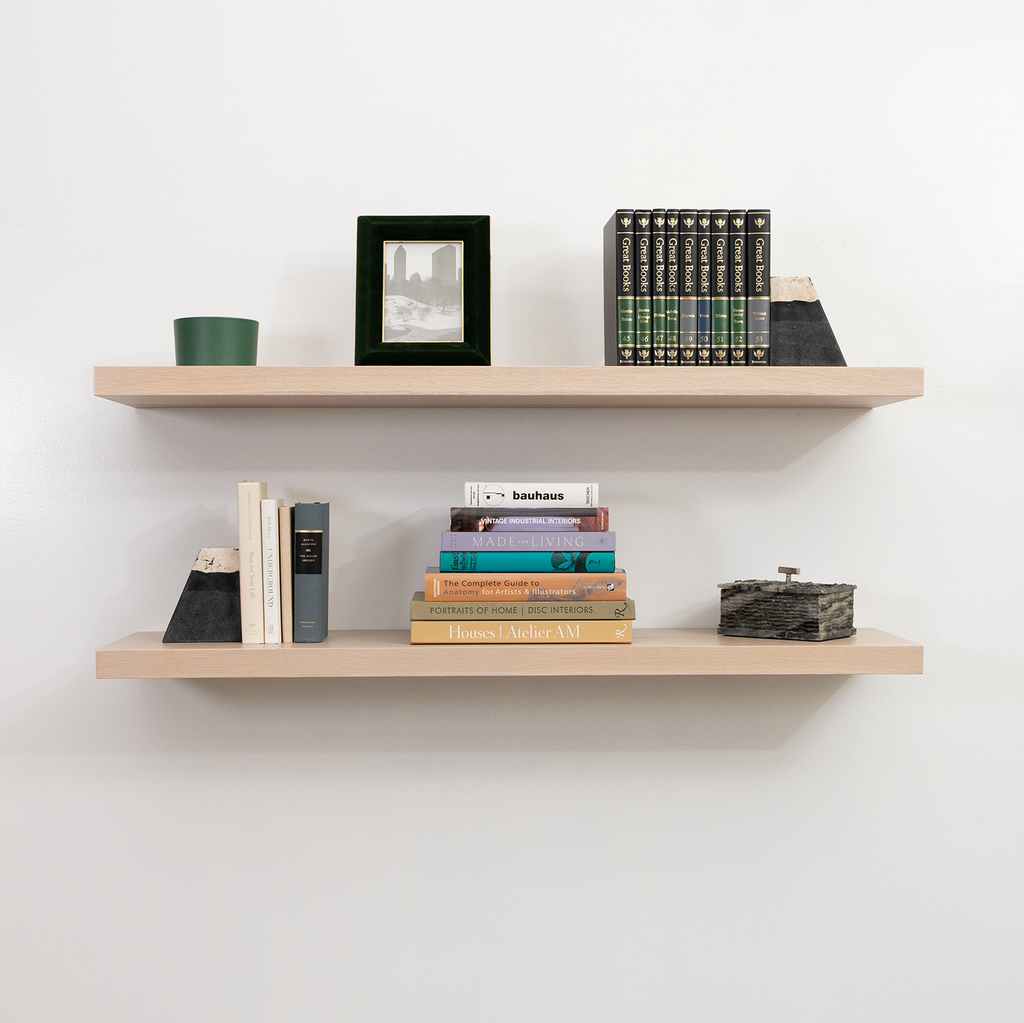 Two wooden floating shelves with books and decorative items against a white wall