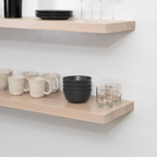 Wooden shelves with ceramic mugs, bowls, and glasses against a white wall.