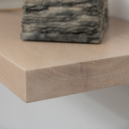 Close-up of a wooden floating shelf with a stone sculpture on a neutral background
